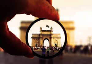 Artistic view of the Gateway of India through a camera lens filter with vibrant colors and bustling crowd.